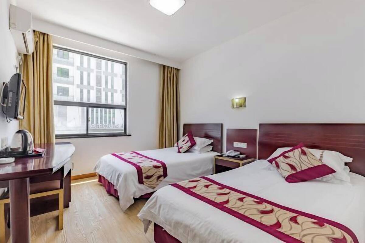 A hotel room with two beds, a desk, a chair, a TV, and a window with curtains.