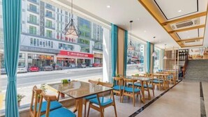 Een modern hotelinterieur met glazen tafels en stoelen, grote ramen met gordijnen en uitzicht op de straat.