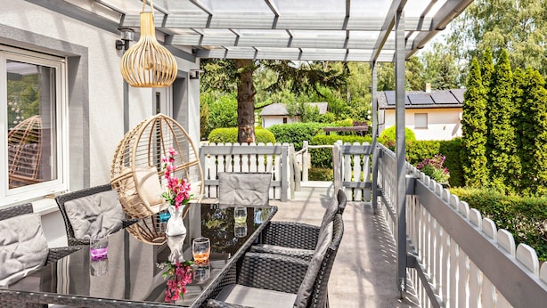 Une terrasse extérieure aménagée avec des meubles en osier, une table en verre et des lampes en osier suspendues.