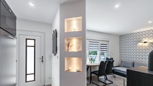 Une cuisine moderne dotée d’un four encastré, un coin repas avec une table et des chaises, et un espace de vie agrémenté d’un canapé et d’un mur décoratif.