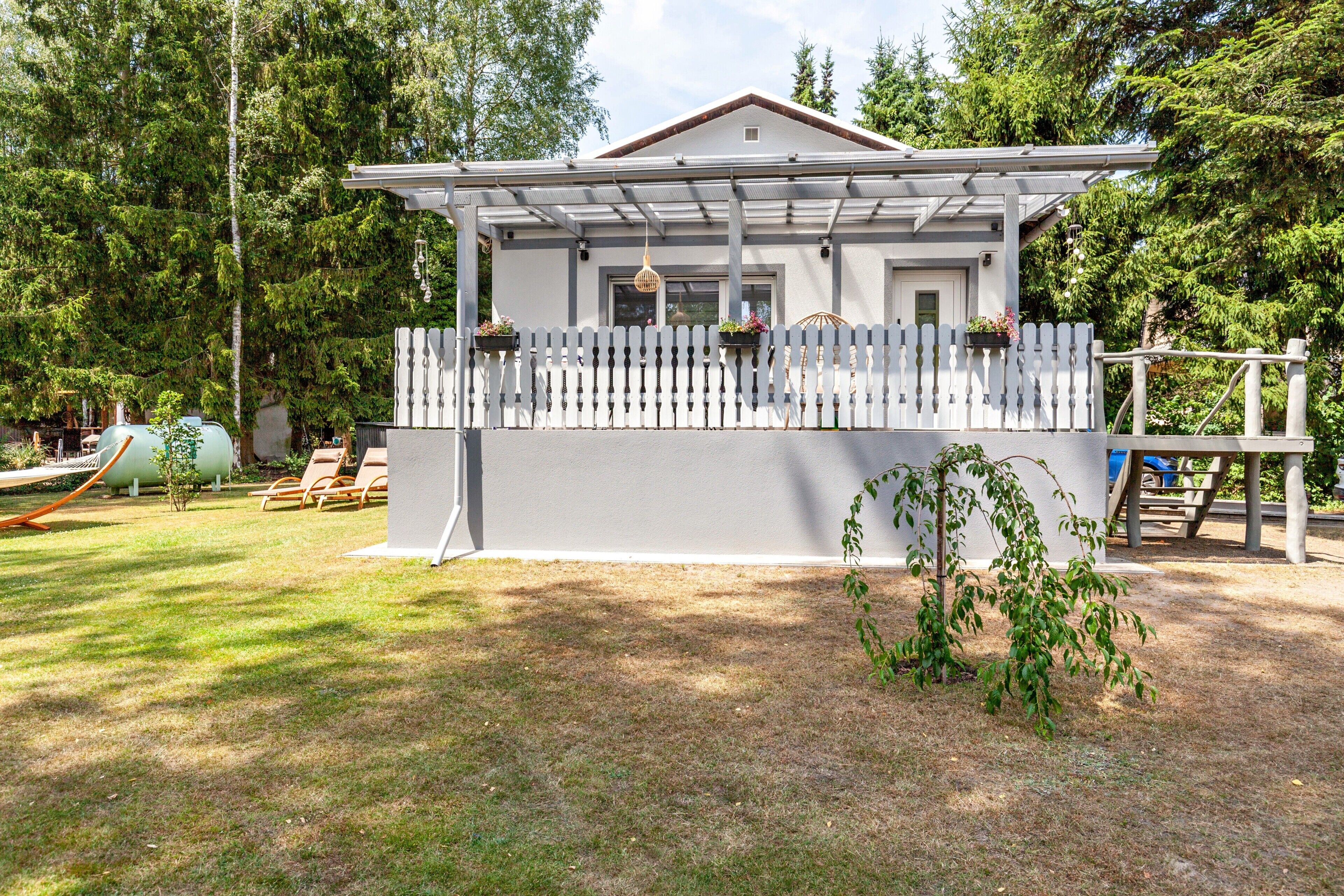 Ein Haus mit weißer Fassade, einer Veranda mit weißem Zierzaun und einem kleinen Garten.