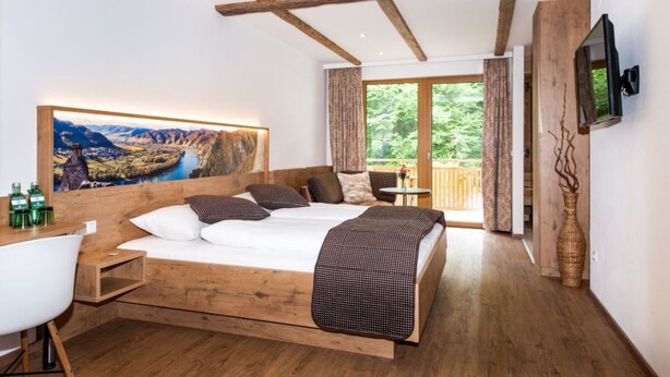 A bedroom with a large bed, wooden beams, a TV, a painting, and a balcony with a view. - Weißes Rössl (Muehldorf)