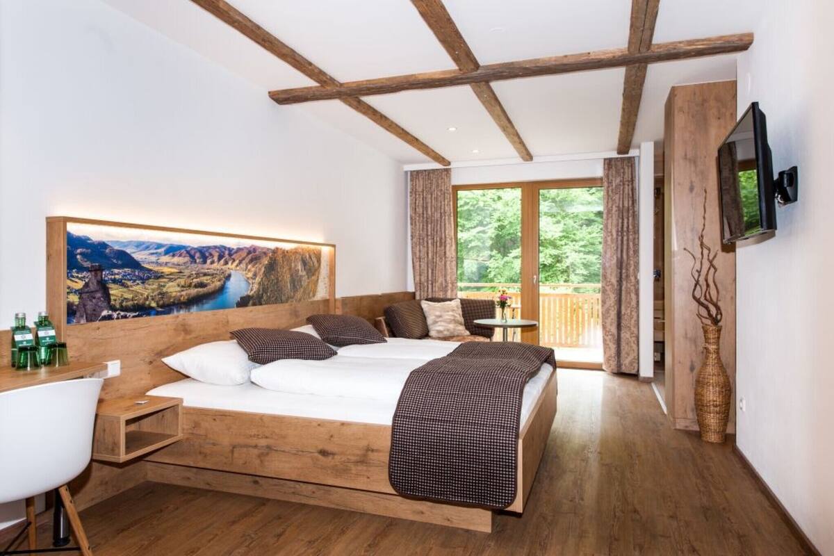 Une chambre avec un grand lit, des poutres apparentes, une télévision, un tableau et un balcon avec vue.