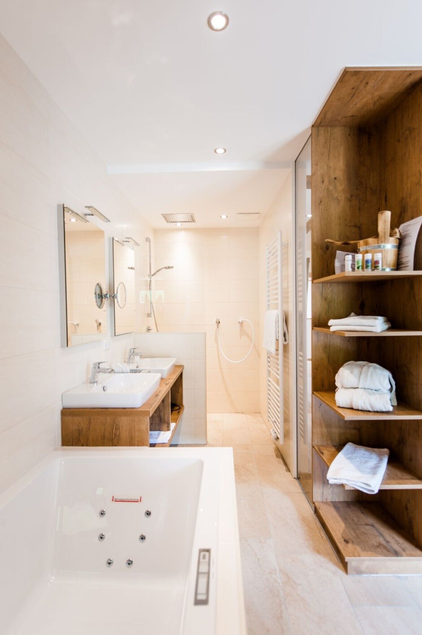 A modern bathroom with a large bathtub, two sinks, a wooden vanity, and a shower area.