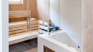 A modern bathroom with a glass-enclosed sauna, a freestanding bathtub, and a wooden bench. - Weißes Rössl (Muehldorf)