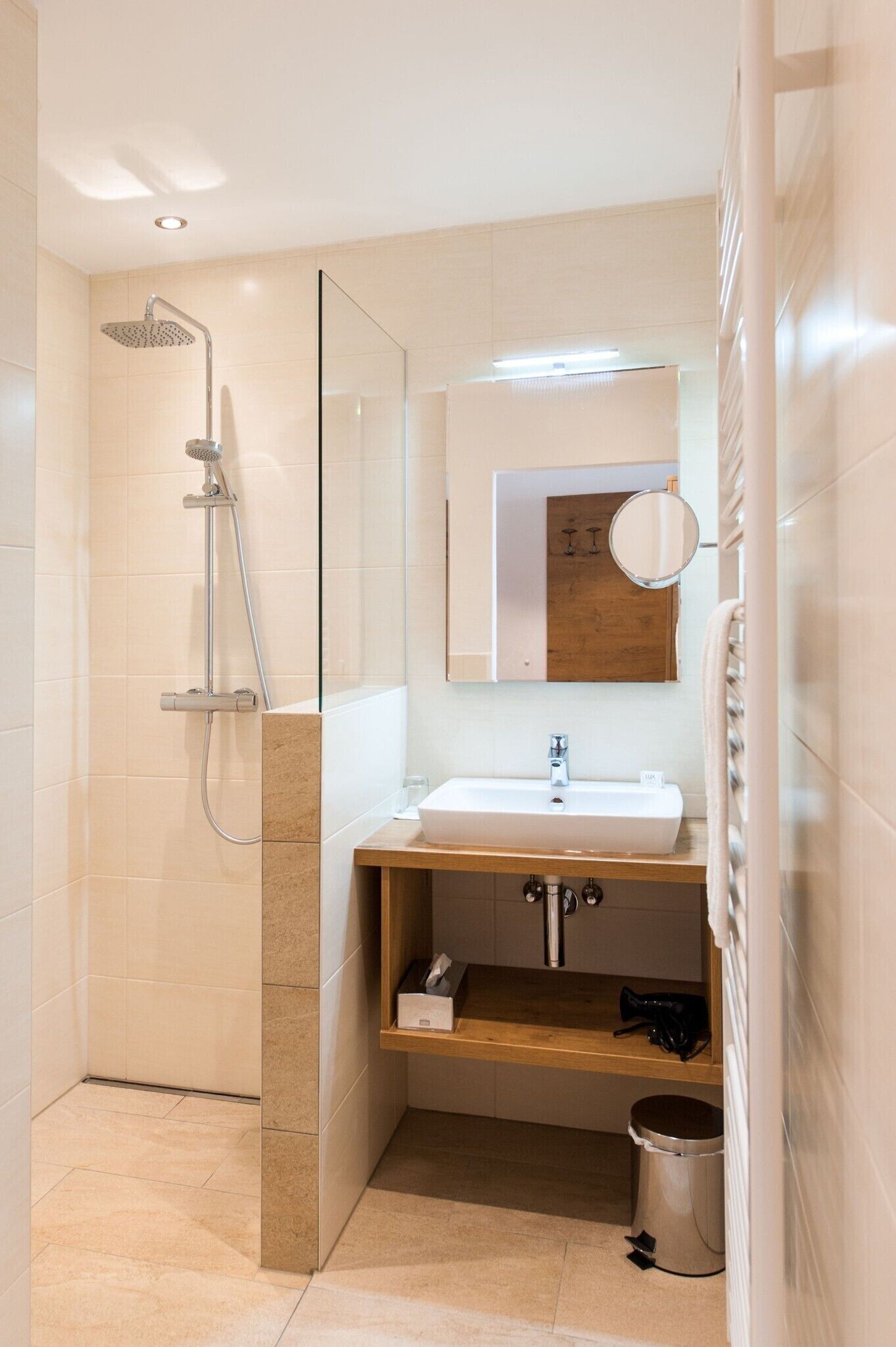 Un baño moderno con cabina de ducha de vidrio, un lavamanos, un espejo y un estante pequeño.