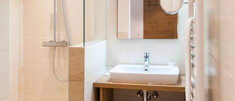 Un baño moderno con cabina de ducha de vidrio, un lavamanos, un espejo y un estante pequeño.