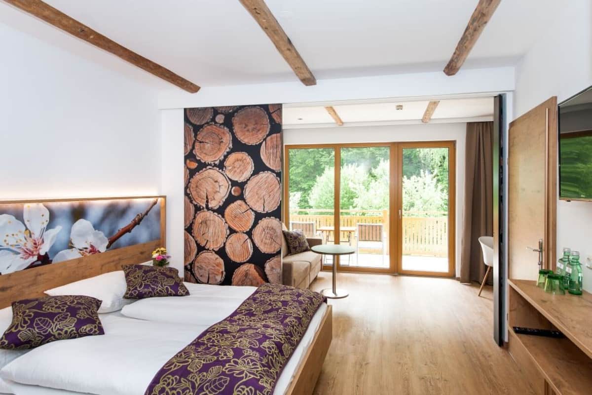 Une chambre à coucher avec un lit, une tête de lit en bois, une grande fenêtre et une vue sur l’extérieur.