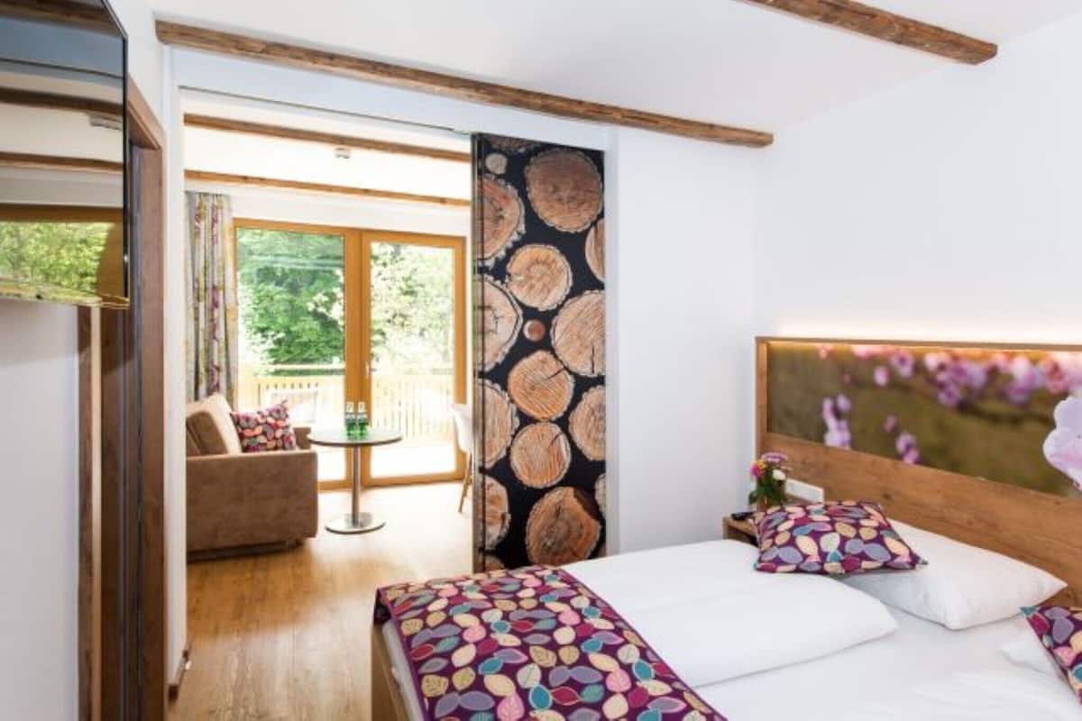 Une chambre à coucher avec un lit, des oreillers, une tête de lit en bois, une fenêtre donnant sur un paysage agréable et une porte menant à un balcon.