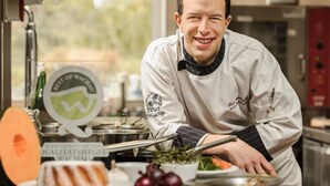 A chef in a kitchen with stainless steel appliances, a window, and a sign indicating a quality assurance seal. - Weißes Rössl (Muehldorf)