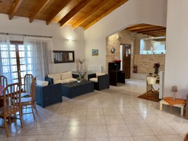 Un amplio salón con un conjunto de sofás, una mesa de comedor con sillas, una chimenea y una cocina visible a través de un vano abierto.