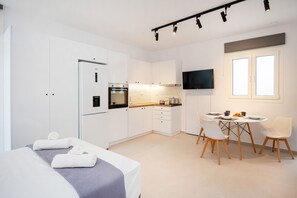 A modern kitchen with white cabinets, a built-in oven, and a dining area with a round table and chairs. - Naxos Mini Cube (Naxos)