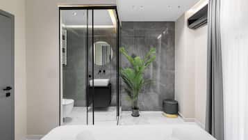 Een moderne badkamer met een glazen douchecabine, een wastafel, een spiegel en een potplant.