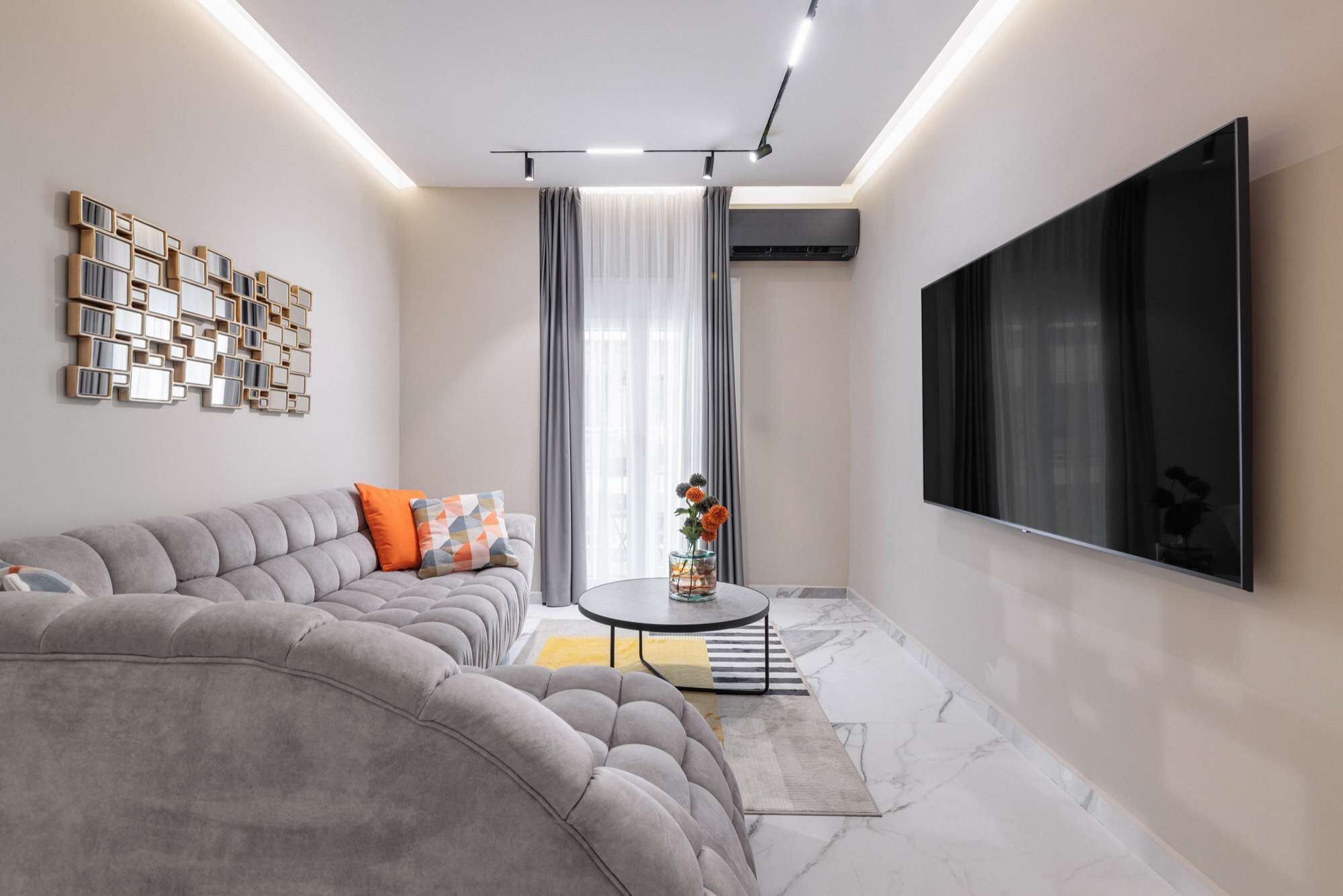 Een moderne woonkamer met een hoekbank, een flatscreen televisie, een decoratief wandkunstwerk en een kleine tafel met een vaas.