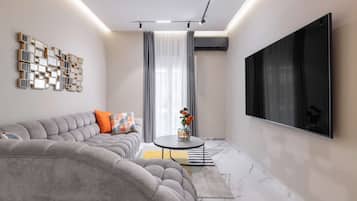 Een moderne woonkamer met een hoekbank, een flatscreen televisie, een decoratief wandkunstwerk en een kleine tafel met een vaas.