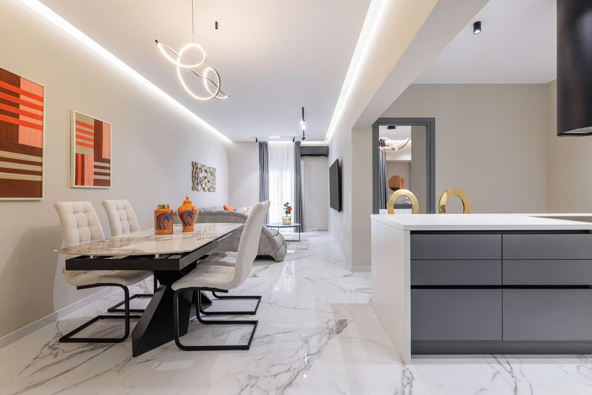 Een moderne keuken met een marmeren aanrecht, een eethoek met een glazen tafel en stoelen, en een zithoek met een bank en kunstwerken.