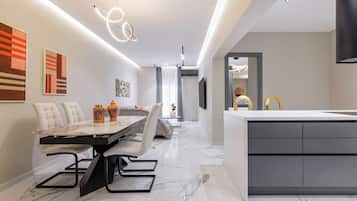 Een moderne keuken met een marmeren aanrecht, een eethoek met een glazen tafel en stoelen, en een zithoek met een bank en kunstwerken.
