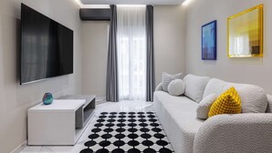 A modern living room with a flat-screen TV, a sofa with cushions, a patterned rug, and artwork on the walls. - Vesper Martini: 2BD Modern Apartment in the center (Thessaloniki)