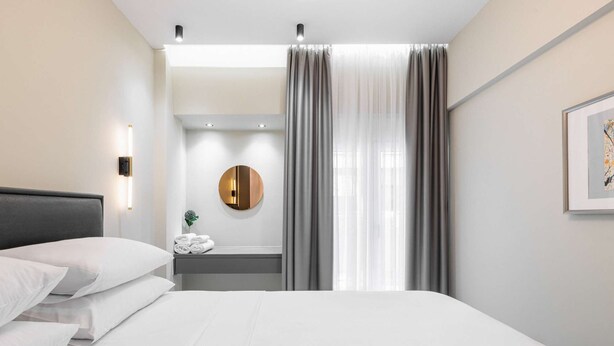 A hotel room with a bed, a bedside table with a lamp, a round mirror, and a framed picture on the wall. - Vesper Martini: 2BD Modern Apartment in the center (Thessaloniki)