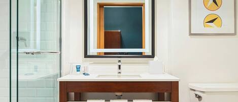 Un baño moderno con cabina de ducha de vidrio, tocador de madera con espejo y un inodoro.