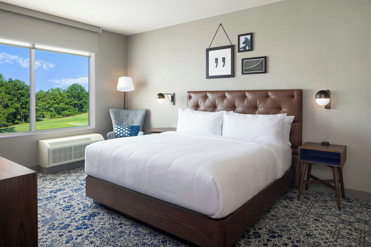 A hotel room with a large bed, a chair, a bedside table, and a view of a golf course.