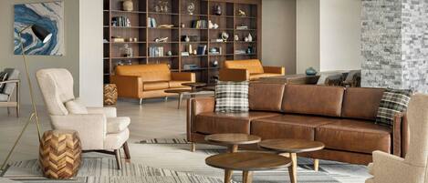 A modern living room with leather sofas, a wooden herringbone side table, and a large bookshelf filled with books and decorative items.