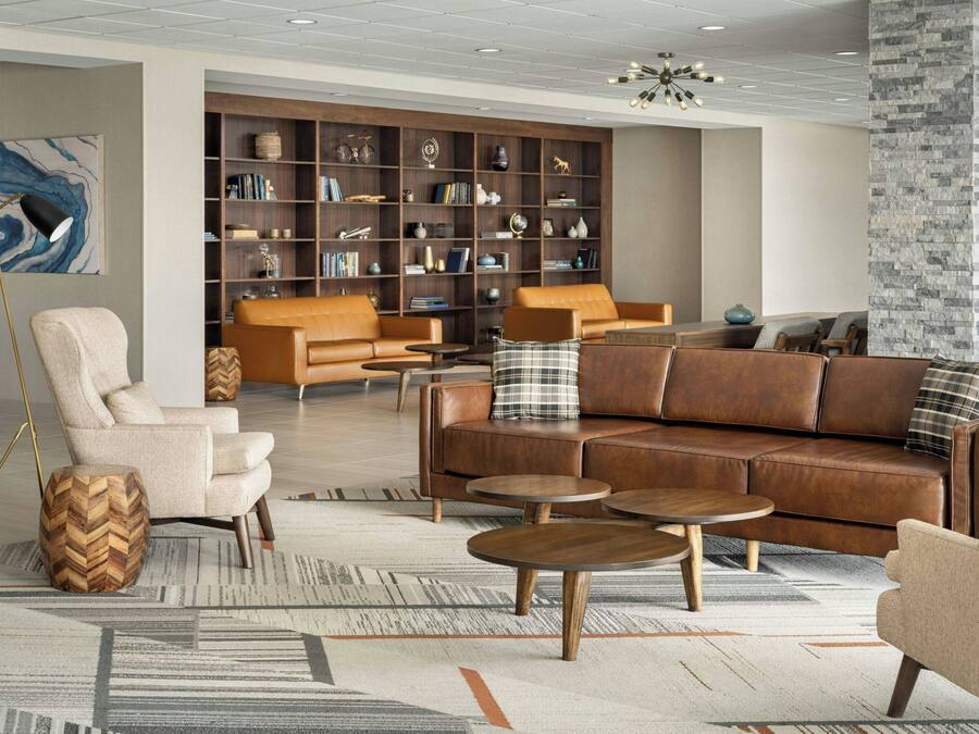 A modern living room with leather sofas, a wooden herringbone side table, and a large bookshelf filled with books and decorative items.