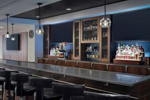 Una zona de bar con una barra larga, taburetes, luces colgantes y estantes con botellas.