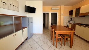 Et køkken med spisebord, stole, køleskab, mikroovn og et TV ophængt på væggen.