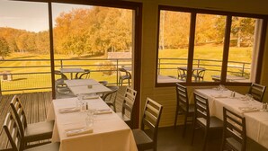 Un comedor interior con mesas preparadas para dos, amplias ventanas que ofrecen vistas a un campo de golf.
