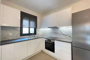 Cocina moderna con armarios blancos, horno negro, refrigerador de acero inoxidable y una salpicadera de mármol.