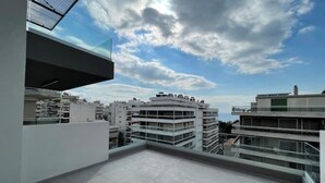 Eine Dachterrasse mit freiem Blick auf umliegende Gebäude und einem teils bewölkten Himmel.