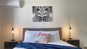 Ein Schlafzimmer mit einem Bett, zwei Nachttischen, einer Wand-Klimaanlage und einem Wandbild.
