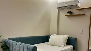 Une chambre moderne avec un canapé-lit, une petite plante, un miroir et un luminaire au plafond.