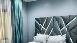 Un dormitorio moderno con cama, cortinas y cabecera.