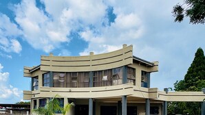 Un edificio de dos plantas con fachada curva, un patio empedrado y un pequeño césped.