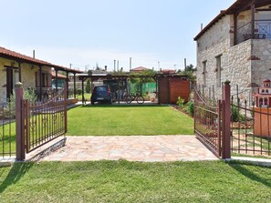 A stone building with a tiled entrance, a car parked in the background, and a bicycle leaning against the building. - Villa Trifon by RentalsPro - Nea Potidaia Halkidiki (Potidaia)
