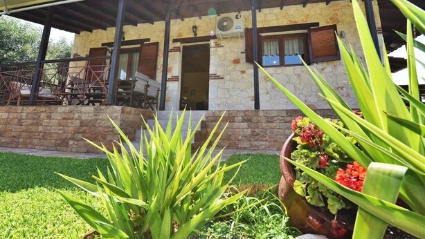 Un bâtiment en pierre avec un toit en tuiles, un patio couvert et un jardin agrémenté de plantes et de fleurs.