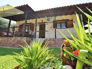 Un bâtiment en pierre avec un toit en tuiles, un patio couvert et un jardin agrémenté de plantes et de fleurs.