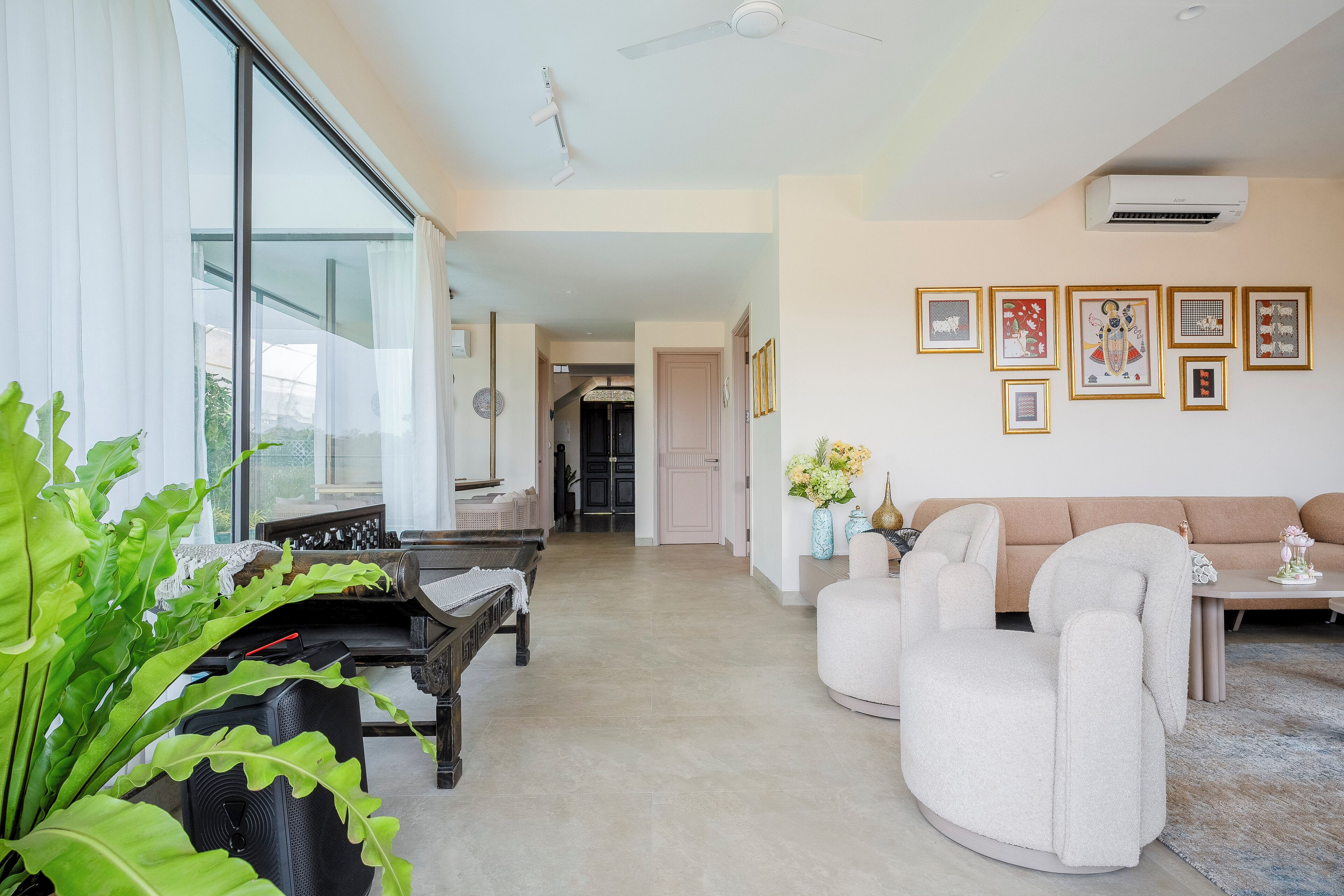 Uma sala de estar espaçosa com um sofá, poltronas, uma mesa de centro e um piano. Há obras de arte emolduradas na parede e uma grande janela com cortinas.