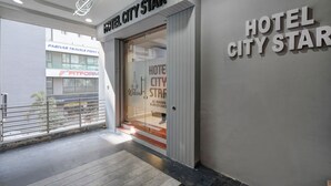 Entrada de hotel con diseño moderno, que incluye puerta de cristal, barandilla de metal y un cartel que dice 'Hotel City Star'.