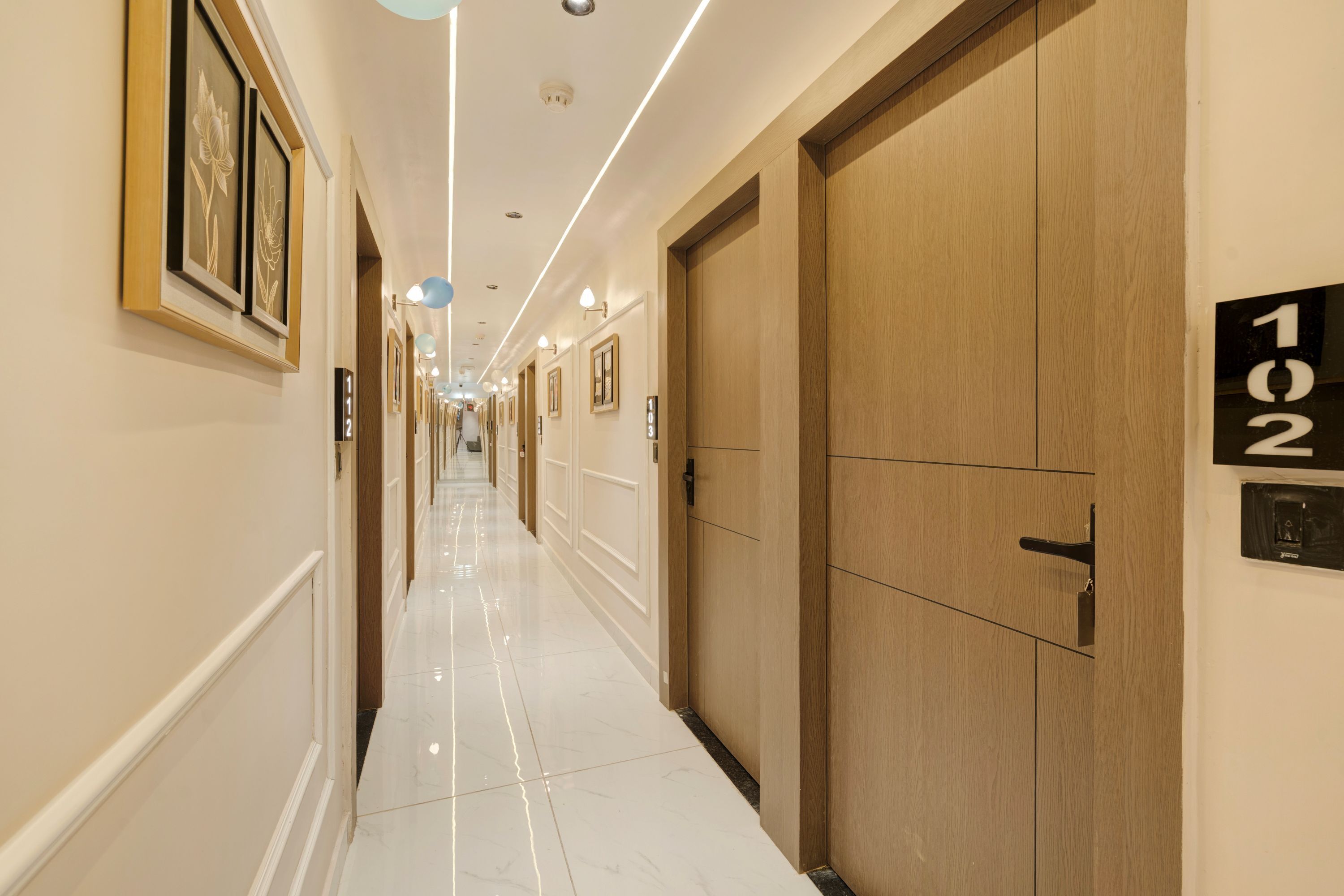 A hotel hallway with a polished floor, wooden doors, and framed artwork on the walls.