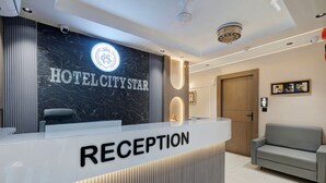 Zona de recepción de hotel con una pared de mármol, mostrador de recepción con la etiqueta 'RECEPTION' y un sofá.