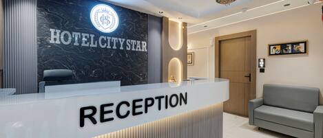 A hotel reception area with a marble wall, a reception desk labeled 'RECEPTION,' and a sofa.