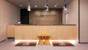 A reception desk with a wooden panel wall, overhead lighting, and a wooden bench in the foreground. - Grand Hostel LDK Osaka Shinsekai - Hostel (Osaka)