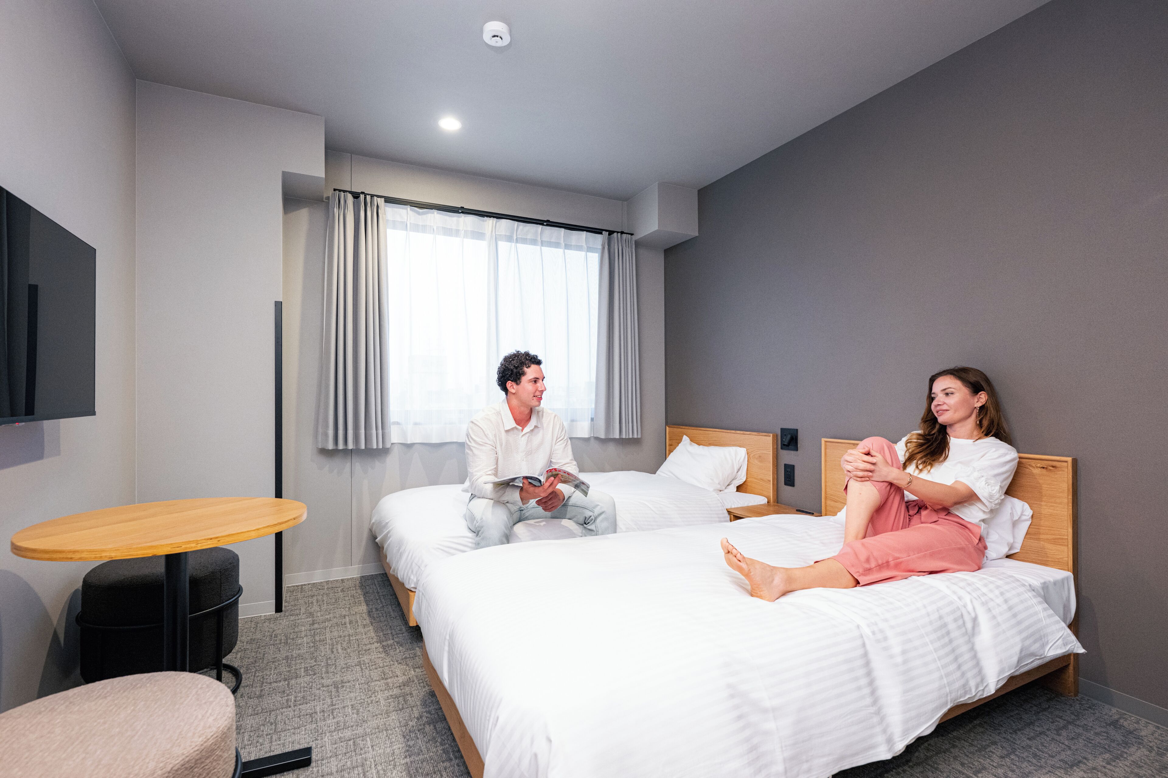 Habitación de hotel con dos camas, una mesita redonda y un televisor montado en la pared.