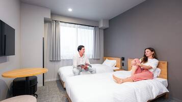 Habitación de hotel con dos camas, una mesita redonda y un televisor montado en la pared.
