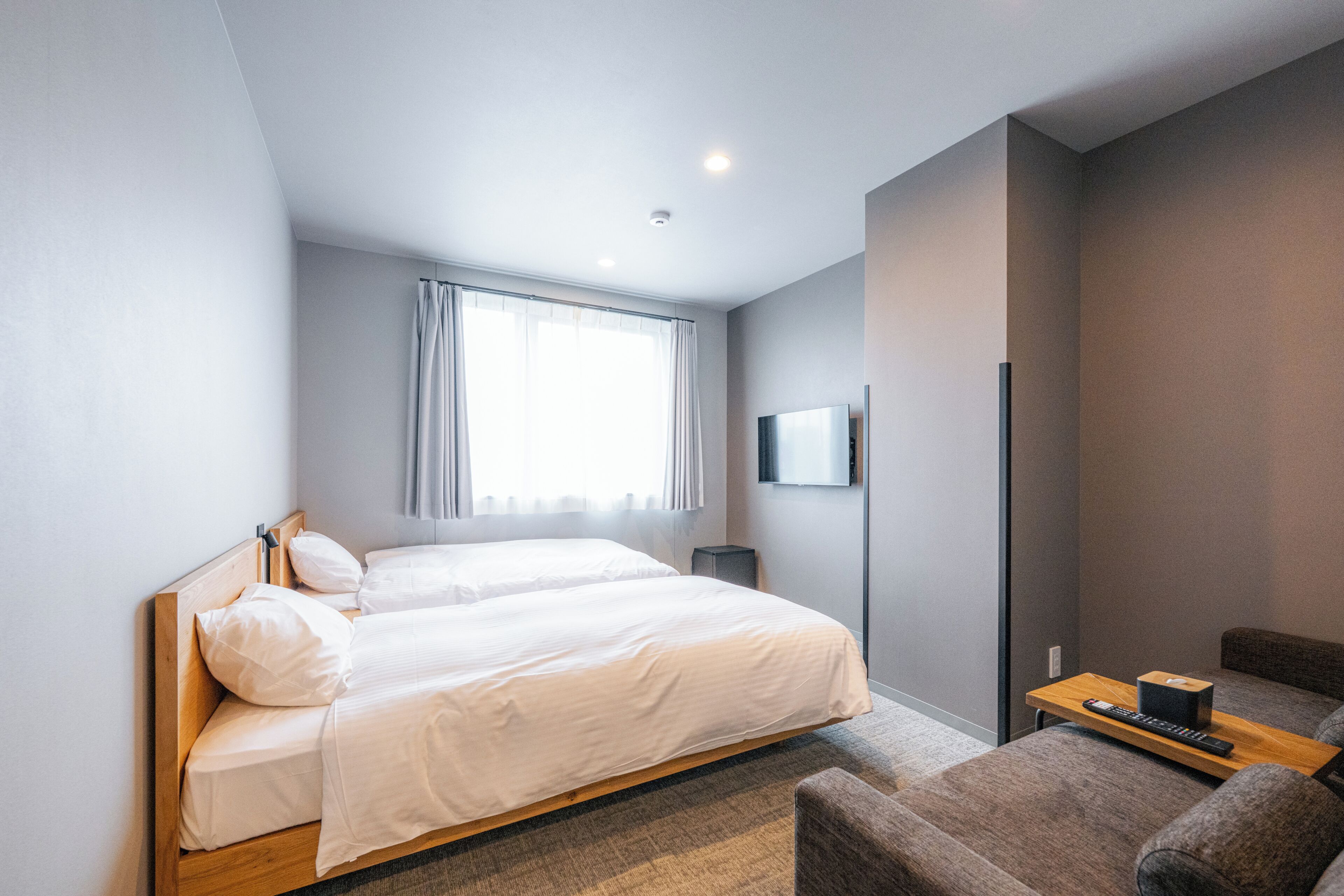 Habitación de hotel con cama doble, televisor montado en la pared, una mesita con un control remoto y un sofá.