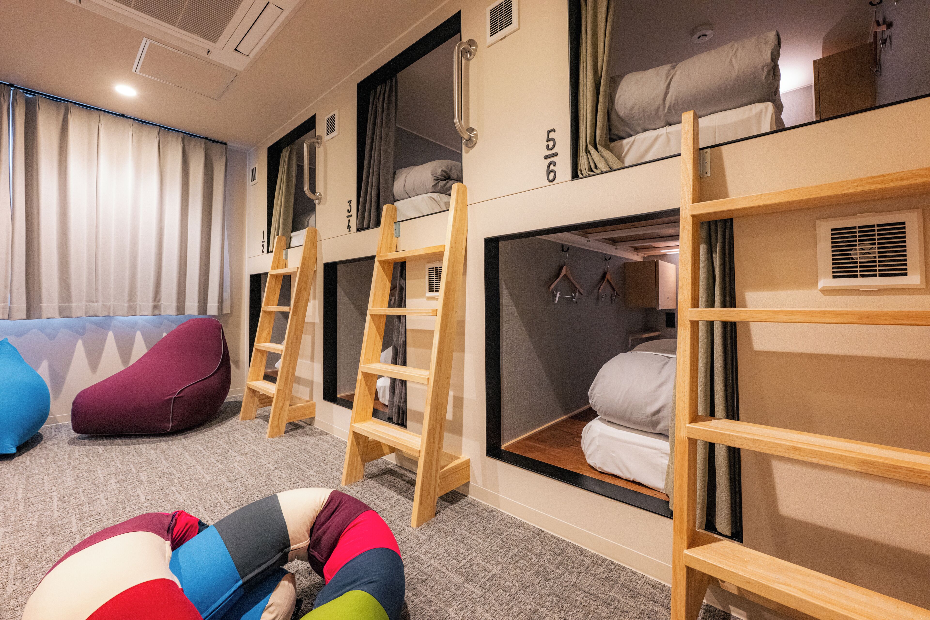 Een slaapzaal met stapelbedden, een trapje, een kapstok en een relax fauteuil.