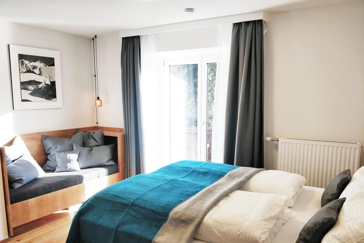 A bedroom with a bed, a wooden bench, a radiator, and a window with curtains.